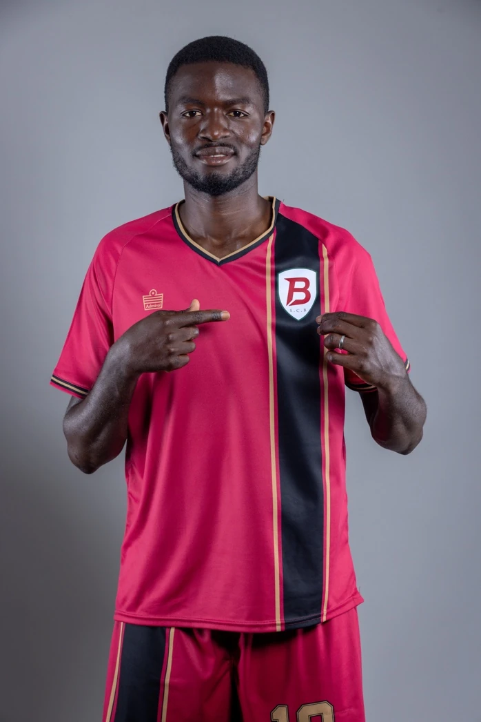 SC Brooklyn player pointing to the crest on the crimson home kit